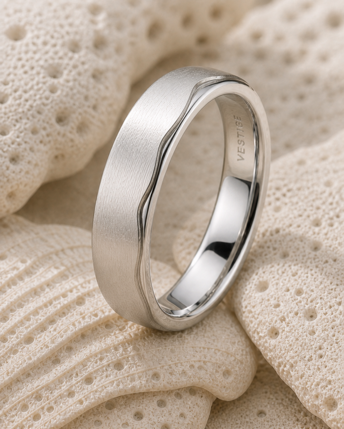 Coastal Ring III standing among pale sculptural coral forms, showing its brushed surface, polished asymmetric edge and mirror-polished interior.